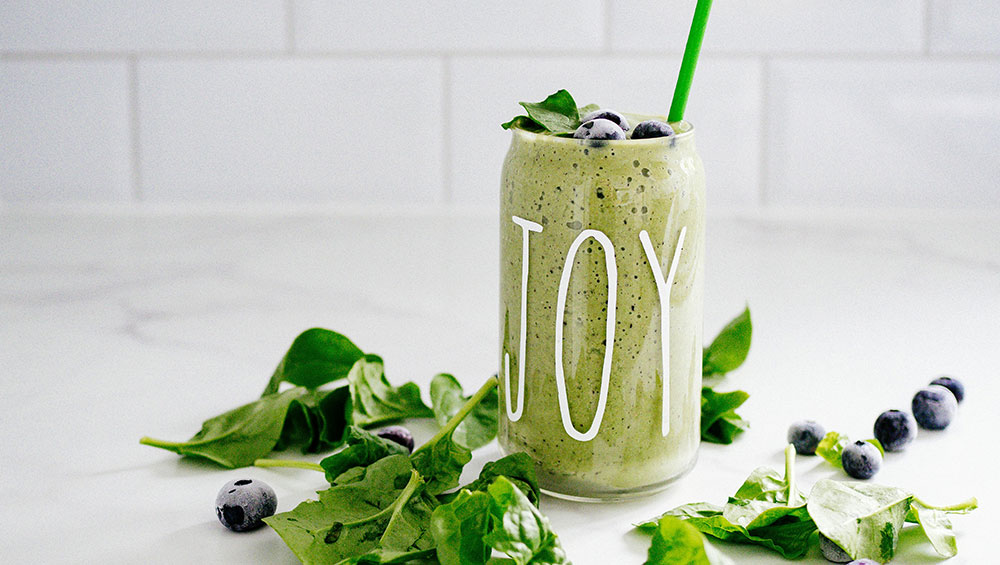 A-green-smoothie-in-a-glass-on-a-table-with-the-words-JOY